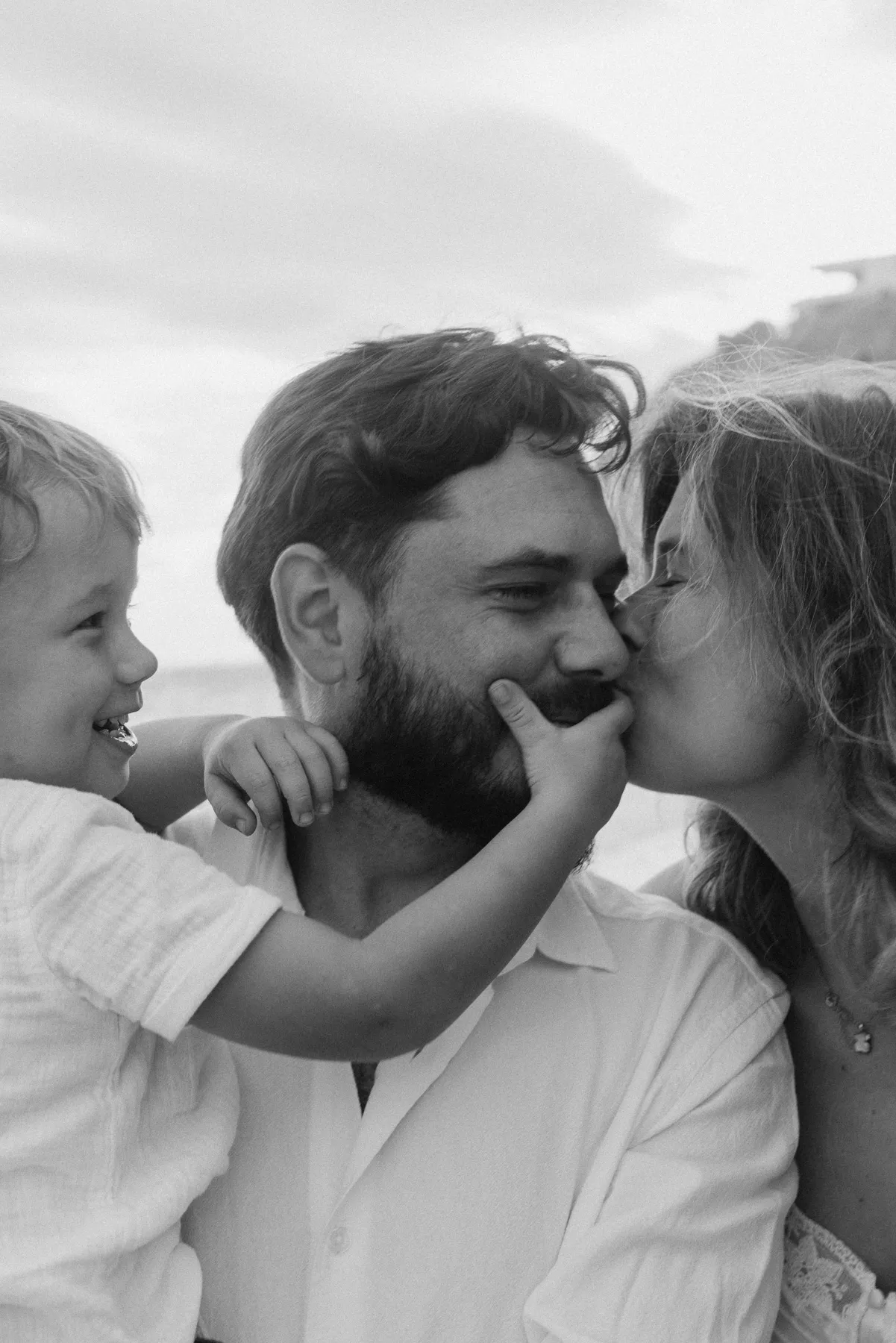 Kind küsst den Vater, die Mutter lacht – Familienfoto in Schwarzweiß