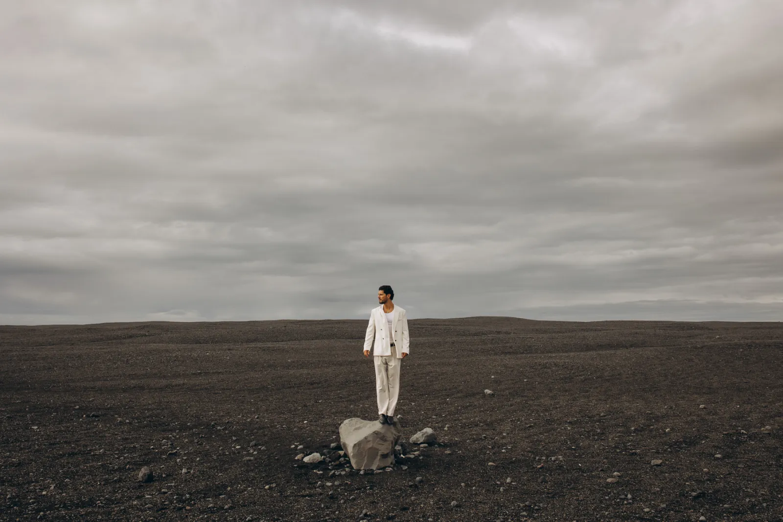 Man in a light suit alone in a wide, dark landscape