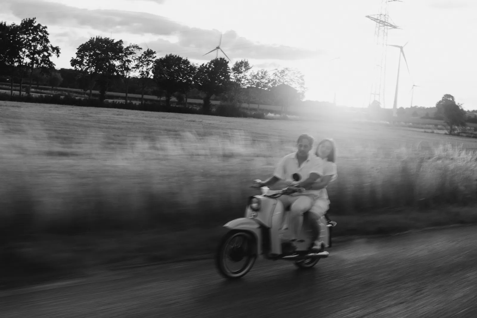 Couple riding a scooter along a country road, black and white