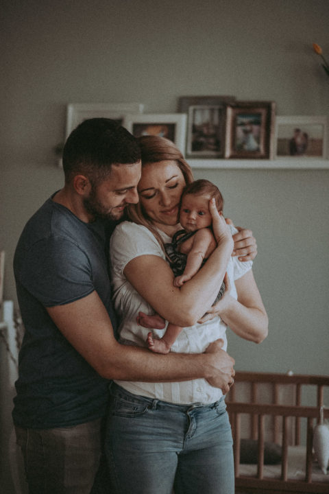 Newborn Shooting, Mann und Frau stehen eng umschlungen mit einem Neugeborenen auf dem Arm im Kinderzimmer