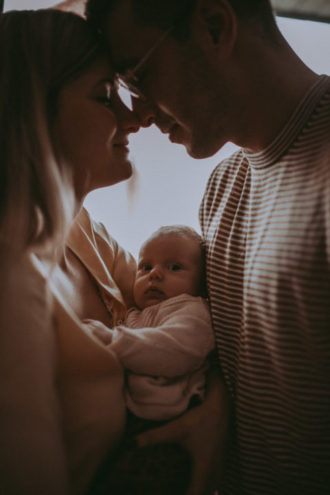 Newborn Shooting, Paar steht dicht bei einander und hält ein Baby zwischen sich auf dem Arm