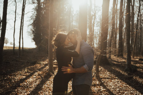 Paarshooting bei Sonnenuntergang im Wald. Paar umarmt sich, Gesichter berühren sich, Frau schwanger